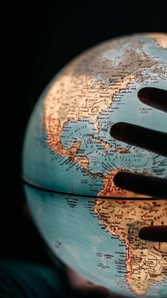 A stock image of a dark hand is turning a glowing globe the background is also black to symbolize  what is astrocartography and travel astrology 