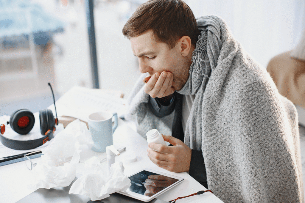 A Man ill at a table with tissues, pills, a mug, a shawl wraped around him as he takes his medication to show stages of a mercury retrograde