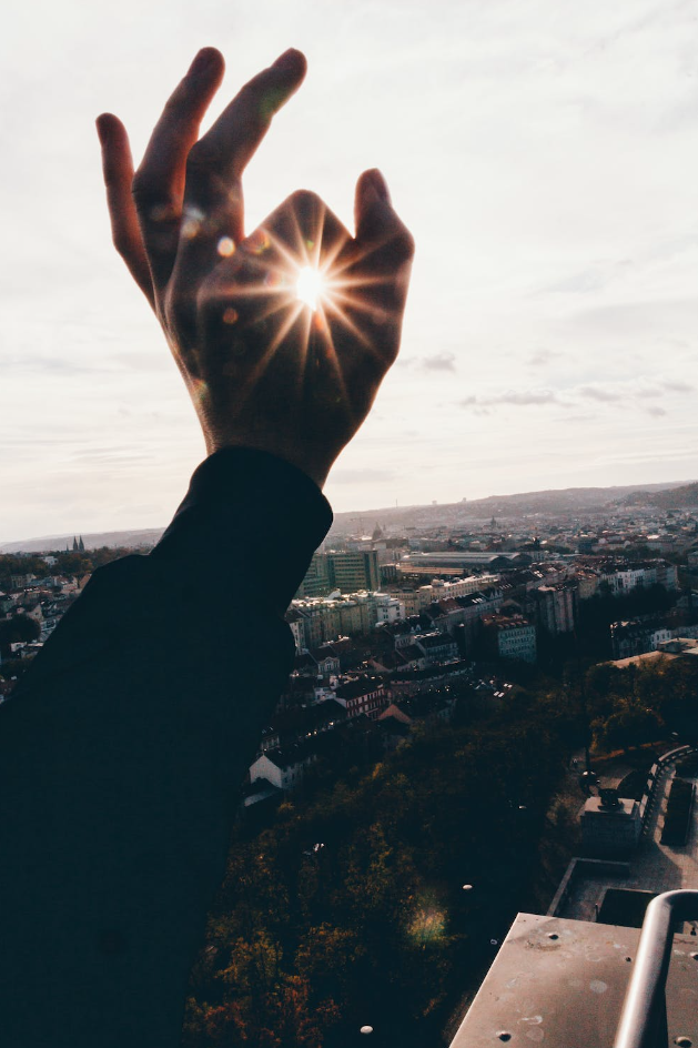A person on a rooftop makes 5he okay sign with their hand. And through the fingers you see the light of the sun to symbolise stealing the sun