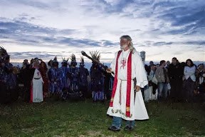 A man in blue jeans with a long white robe and red scarf, white beard at Summer Solstice at Stonehenge to mark Arthur Pendragon, a self-proclaimed Druid King and reincarnation of King Arthur, who led solstice sunset services.