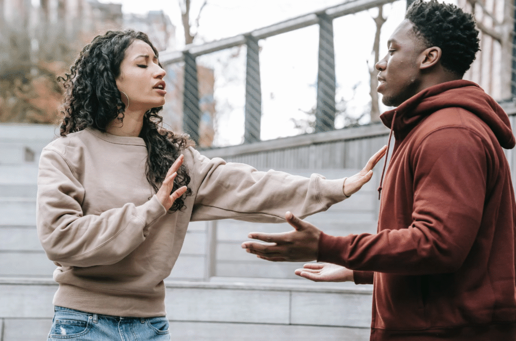 A photogragh of an interracial couple arguing . The man has both hands in the air whilst the woman halts him to stop talking to symbolise a man saying, "I really like you, but..."