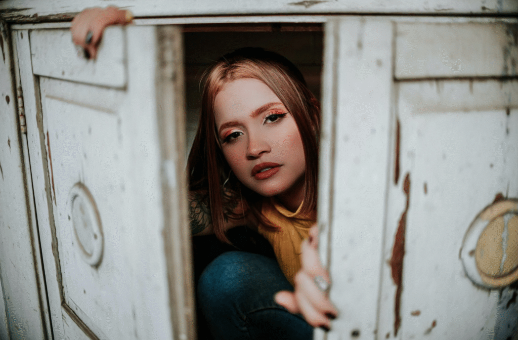 A photograph of a woman peaking out of a cupboard to represent being hidden