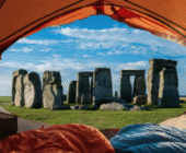 A photgraph of an opened orange-coloured tent with one blue and one orange sleeping bag inside the tent looking out to Stonehenge when I slept at Stonehenge astrocartography.