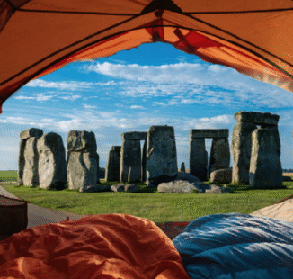A photgraph of an opened orange-coloured tent with one blue and one orange sleeping bag inside the tent looking out to Stonehenge when I slept at Stonehenge astrocartography.