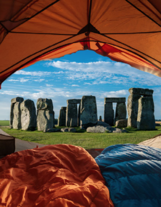 A photgraph of an opened orange-coloured tent with one blue and one orange sleeping bag inside the tent looking out to Stonehenge when I slept at Stonehenge astrocartography.