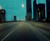 Moving image of cars and buses driving over an overpass/flyover, driving past modern tall buildings to depict the 3rd house in astrology and transportation