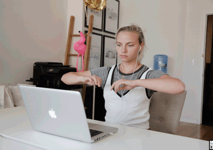 A moving image of a woman at her desk with earphones watching her MacBook and doing exercise.
