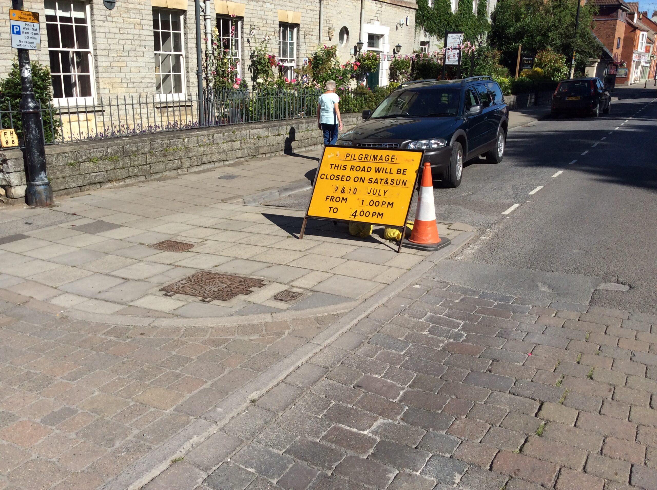 My phtograph of a road floor sign in Glastonbury reads, Pilgrimage: the Road will be closed 9 & 10 July From 1:00 pm to 4:00pm