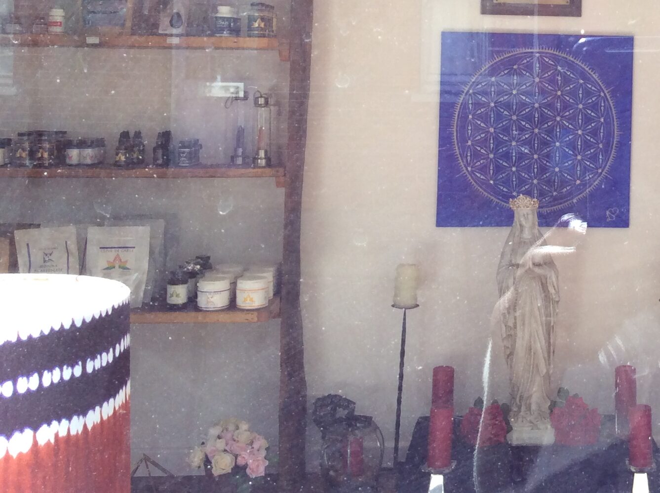 My photograph of outside a shopfront in Glastonbury looking through the glass at a purple and gold Seed of Life sacred geometry print on the wall.