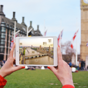 A photoshopped potography iPad Mini in the hands of a woman outdoors the house of Parliment the image in the ipad is of another side of Parliment near the river with captions of where I was born