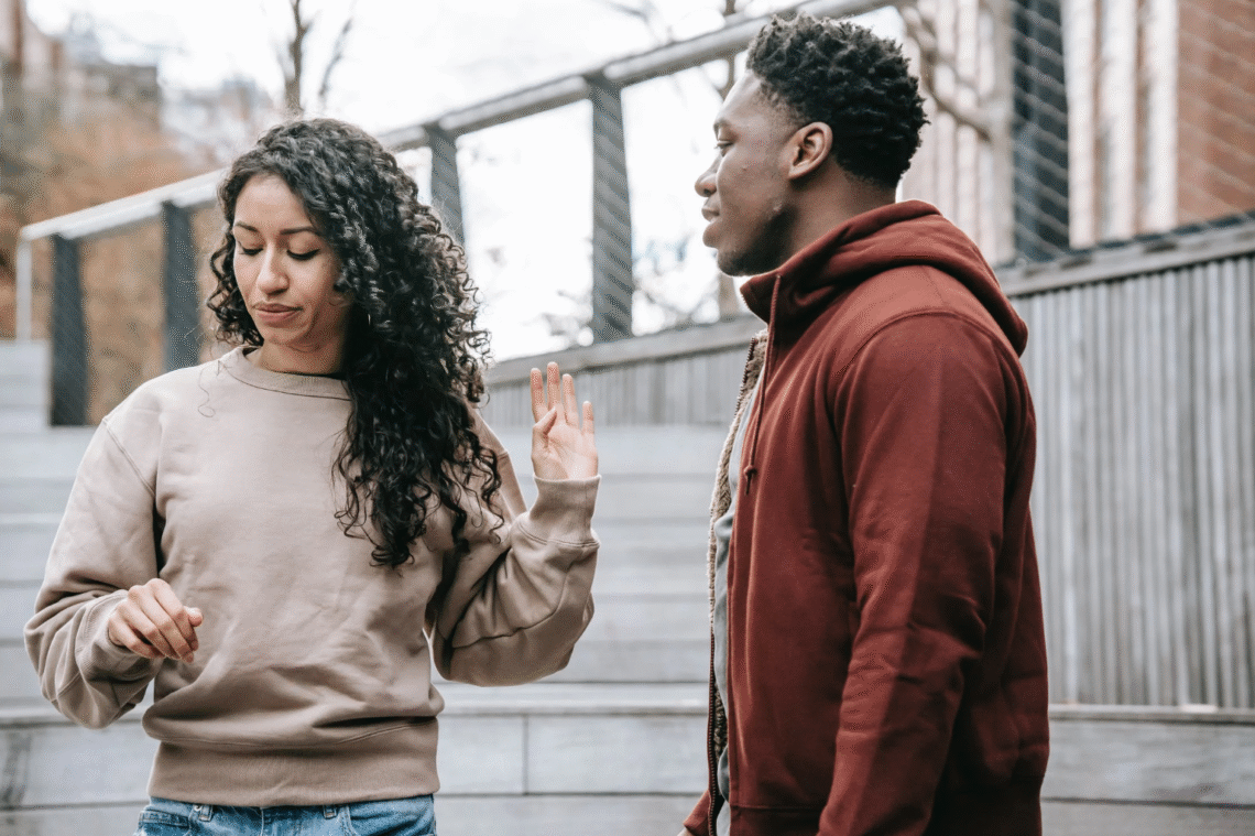 Photograph of an interracial heterosexual couple outside; her hand is saying 'stop'.