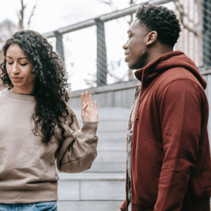 Photograph of an interracial heterosexual couple outside; her hand is saying 'stop'.