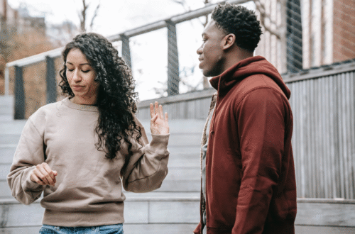 Photograph of an interracial heterosexual couple outside; her hand is saying 'stop'.